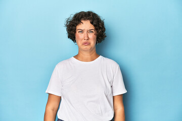 Young Caucasian woman with short hair blows cheeks, has tired expression. Facial expression concept.