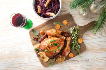 Roast chicken with fruits and herbs, red cabbage and wine on a wooden board, pine branches and...