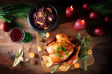 Roast chicken with red cabbage and wine on dark rustic wood with candles and Christmas decoration,...