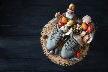 Winter boots filled with a chocolate Santa, treats and Christmas decoration on dark blue wood for...