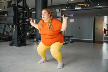 Fototapeta na wymiar Overweight woman having fitness workout squatting with body bar training equipment