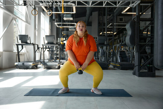 Overweight obese woman squatting with kettlebell while training at gym