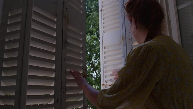 Young red haired woman opening wooden shutter