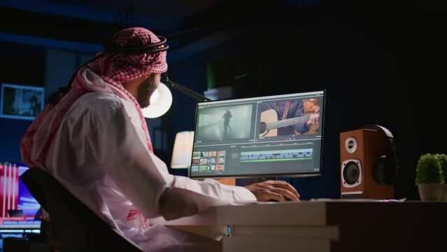 Arabic colorist freelancer wearing headphones while editing project, stitching videos together, working with images and sounds. Self employed man processing movie on PC workstation