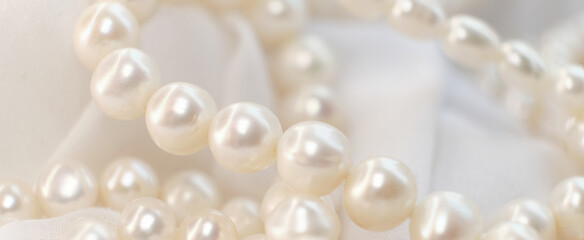 A cascade of pearls rests on a soft, white cloth, their natural luster dimly reflecting light. The...