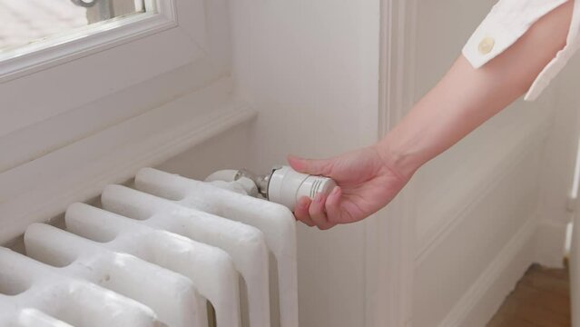 Hand of woman rises up heat level with knob on radiator on cold winter day
