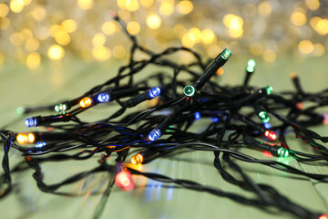 Black garland with colored lights on green wooden background, close up