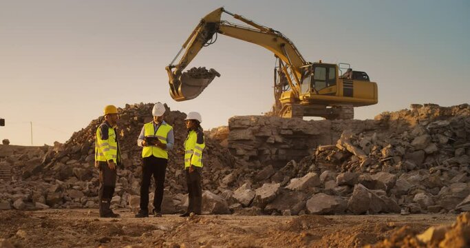 Construction Site With Excavators on Sunny Day: Diverse Team Of Male And Female Specialists Discussing Real Estate Project. Civil Engineer, Architect And Investor Talking About New Apartment Building.