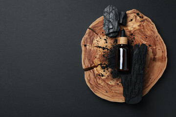 Serum in an amber jar with charcoal, on a wooden slice.