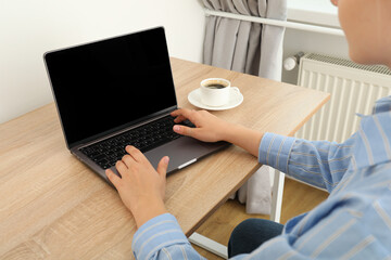 A woman with a cup of coffee is working on a laptop