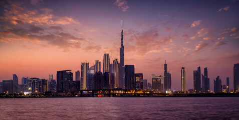 Fototapeta premium Panoramic view of the illuminated skyline of Dubai Business bay with reflections of the modern skyscrapers in the water during dusk time, UAE
