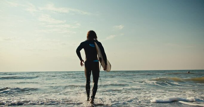 Happy curly male surfer with a yellow surfboard runs into the water and swims to the wave in the sea. Surfer guy runs into the water and starts swimming