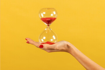 Unrecognizable woman holding hourglass in hand against yellow backdrop - Powered by Adobe