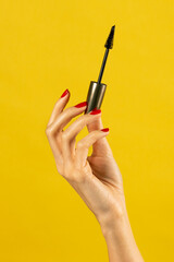 Unrecognizable young woman holding mascara in hand against yellow backdrop