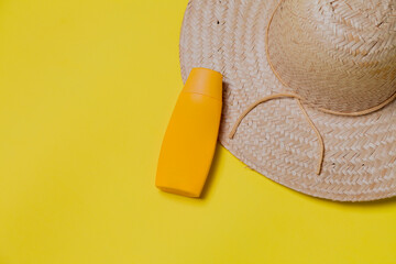 Straw hat on yellow background with sunscreen packaging. Space for text. Hat concept. Sombrero...