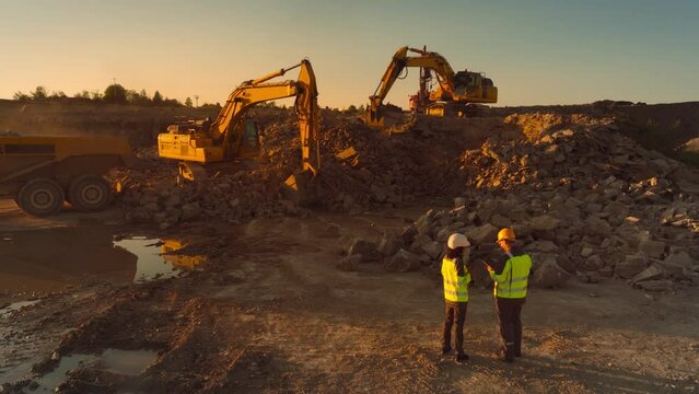 Aerial Drone Shot Of Construction Site On Sunny Evening: Industrial Excavators Digging Rocks And Loading Them Into Truck. Civil Engineer And Inspector Observing Process, Discussing Real Estate Project