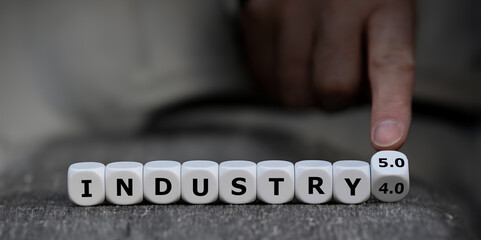Hand turns dice and changes the expression 'industry 4.0' to 'industry 5.0'.