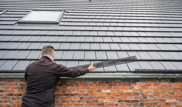 Man puts a gutter mesh to the rain gutter to protect the gutter from leaves..