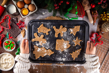 Cooking Christmas cookies family background. Mother and daughter hands top view on cozy wooden background, making gingerbread biscuits with cookie cutters, with New Year Christmas decoration