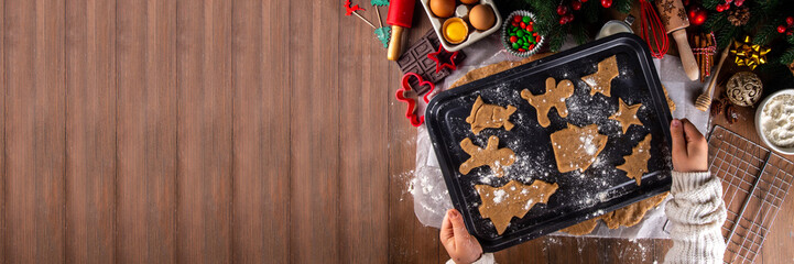 Cooking Christmas cookies family background. Mother and daughter hands top view on cozy wooden background, making gingerbread biscuits with cookie cutters, with New Year Christmas decoration