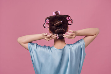 Back view of young woman with hair curlers on pink