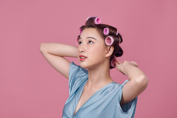 Cheerful young model posing with hair curlers on pink background