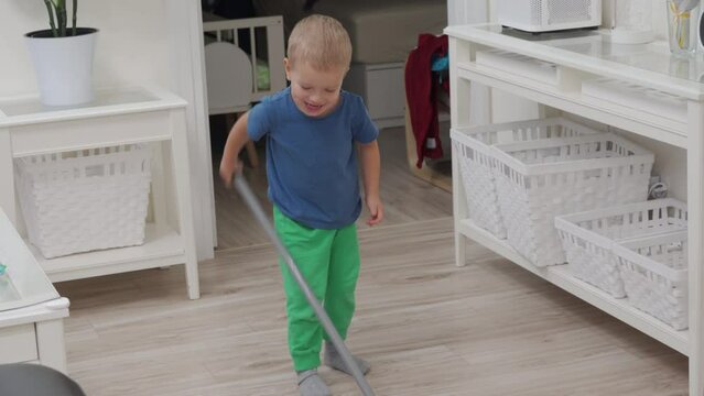 toddler child little boy playing with broom cleaning home, happy child sweeping floor with broomstick