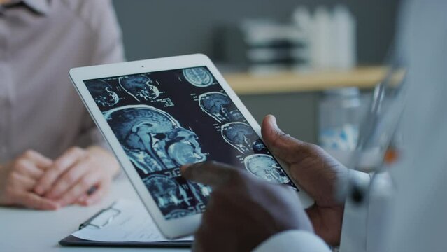 Close up over shoulder shot of unrecognisable doctor looking at tomography results in tablet during appointment with patient in private clinic