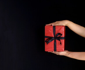 Woman's hands holding red gift box with black ribbon over black background. Black Friday and Boxing Day composition.
