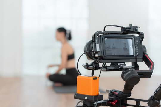 Blogger recording live video tutorial at home. Young woman sitting on yoga mat in lotus position and holding a camera.