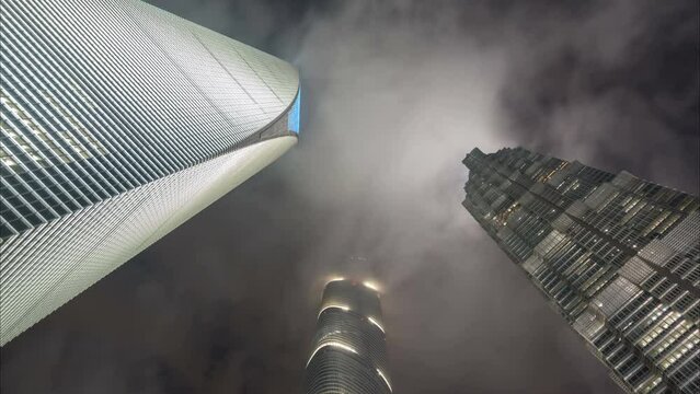 Evening time lapse view of clouds moving over the three iconic skyscraper office towers in the central business district of Shanghai, China
