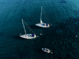 Sailing yachts anchored in blue sea, top view. Sailing yacht on dark background, aerial view.