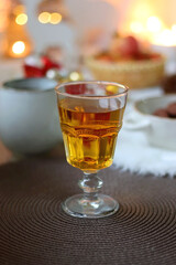 Cup of tea or coffee, glass of wine or juice, bowl of cookies, organic pomegranate, fluffy blanket, pine cones, various Christmas decorations and lit candles on the table. Christmas hygge concept.