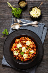 Lasagnette with beef ragu, mushrooms and ricotta cheese in black bowl on dark wooden table with ingredients and seasoning, italian recipe, vertical view from above