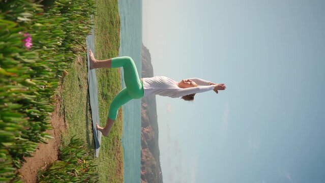 Pensioner woman doing yoga on the beach. Senior woman stands in warrior pose virabhadrasana on ocean shore. Fitness in nature on sunny day. Healthy senior lifestyle. Vertical shot