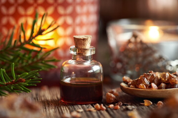 A bottle of myrrh essential oil with spruce branches and candle at Christmas - obrazy, fototapety, plakaty