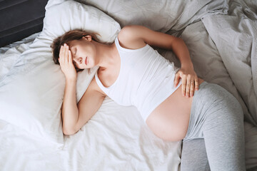 Exhausted pregnant woman suffering from insomnia or pain lying in bed. - Powered by Adobe