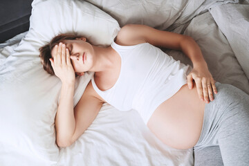 Exhausted pregnant woman suffering from insomnia or pain lying in bed.
