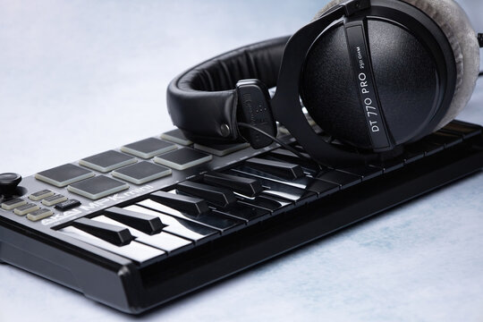 Closed-back headphones of the beyerdynamic dt 770 brand lie on the AKAI MPK mini mk2 midi keyboard, on a light background