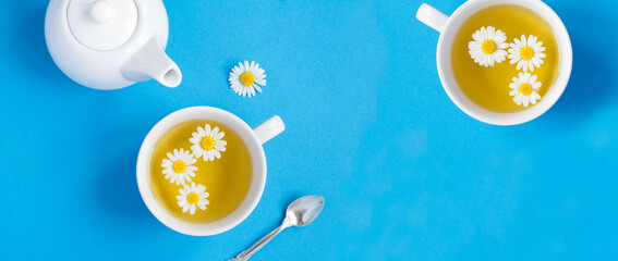 Tea with chamomile flower in the white cups and teapot on the blue background. Top view.