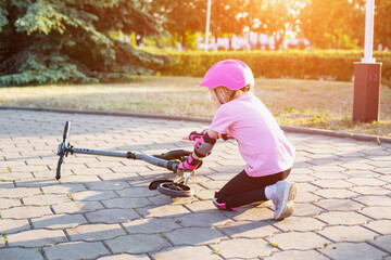 A 7-year-old girl in a pink helmet and protective gear fell off a scooter. The concept of safe riding a scooter and a bicycle without injury. Copy space for text © HENADZY
