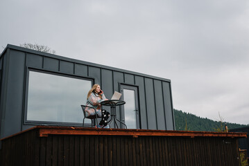 Workplace in country in backyard house in morning. Female talking on phone outdoors. Woman remote work on laptop sitting table with great view mountains. Concept freelance lifestyle. Internet 5G