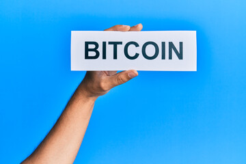 Hand of caucasian man holding paper with bitcoin word over isolated blue background