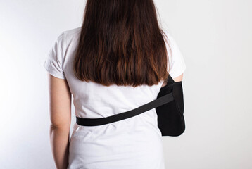 A girl on a white background with a black supporting medical bandage after a dislocation of the...