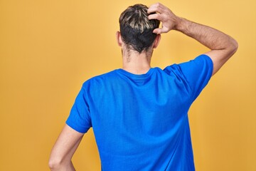 Hispanic man with beard standing over yellow background backwards thinking about doubt with hand on head