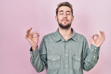 Hispanic man with beard standing over pink background relax and smiling with eyes closed doing meditation gesture with fingers. yoga concept.