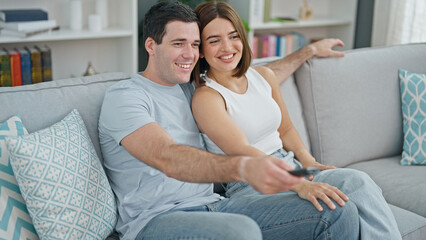 Beautiful couple watching tv sitting on sofa at home