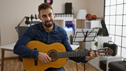 Soulful strumming by smiling young hispanic man, classic melody immersed in music studio performance on acoustic guitar