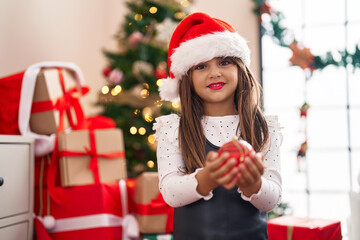 Adorable hispanic girl smiling confident holding christmas ball decoration at home