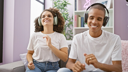 Joyful, confident couple enjoy fun dancing and listening to catchy music while sitting on cozy home...